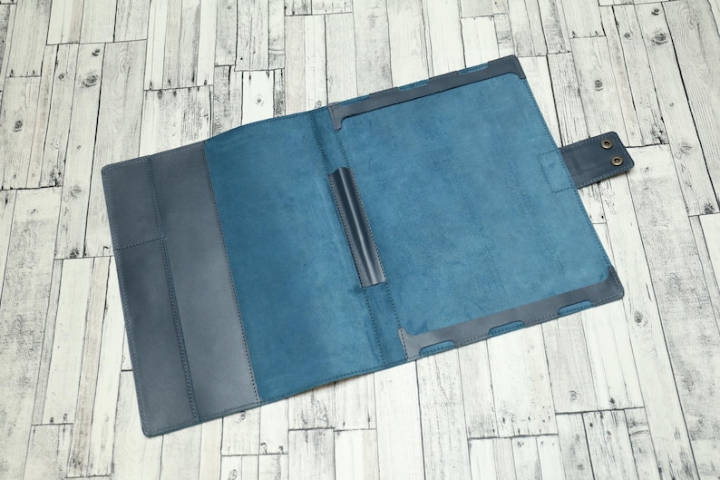 May include: A blue leather notebook with a flap closure and a pen holder. The notebook is open to reveal a blue interior.