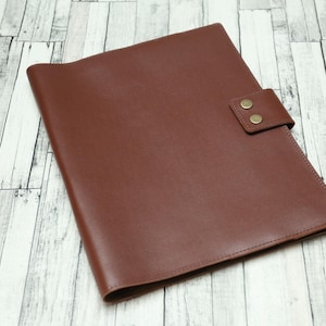 May include: A brown leather folder with a flap closure and two brass button accents.