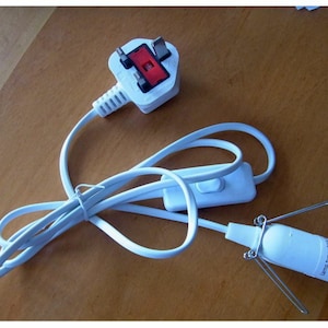 Puede incluir: Un cable eléctrico blanco con un enchufe británico, un interruptor en línea y un portalámparas. El portalámparas está etiquetado como "Lamp Type 230V" y tiene la marca CE.