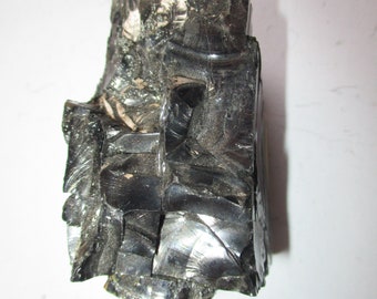 May include: A large, dark gray, irregularly shaped piece of obsidian with a shiny, glassy surface.