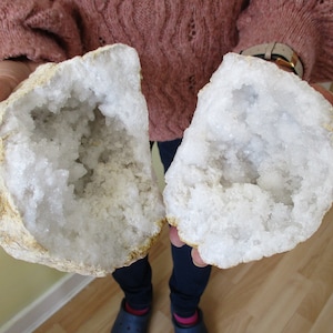 May include: Two halves of a large, white geode with a rough, tan exterior. The inside of the geode is filled with white, crystalline formations.