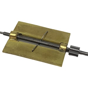 May include: A brass watch winder with a metal rod and a gear on one end. The winder is used to wind a watch by turning the gear.