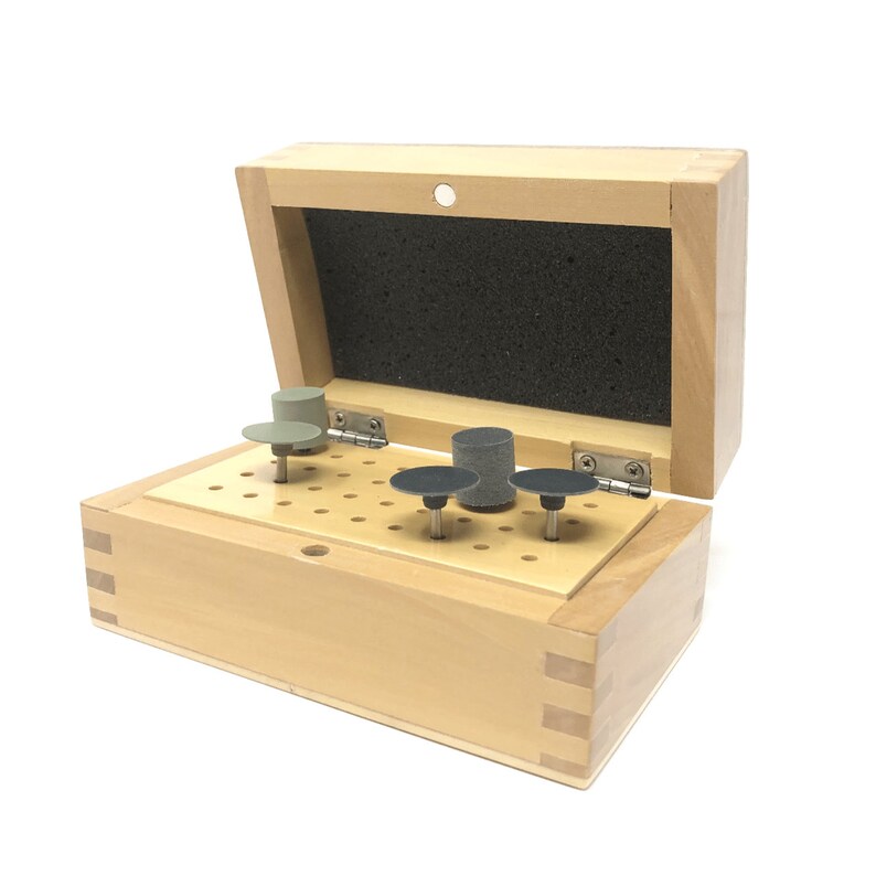 May include: A wooden box with a hinged lid, open to reveal a set of small, round sanding tools. The tools are arranged in a grid of holes in the box's interior. The tools are various shades of gray and black.