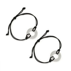 May include: Two black string bracelets with silver metal circle charms. The charms have a hole in the centre.