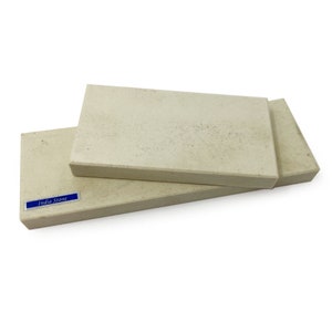 May include: Two rectangular India stone sharpening stones, one stacked on top of the other. The top stone is light beige with a rough texture. The bottom stone is a slightly darker beige with a smooth texture. The label "India Stone" is printed in blue on the bottom stone.
