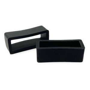 May include: Two black rubber watch strap keepers. The keepers are rectangular with a rounded edge and a slot in the centre.