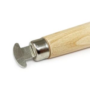 May include: A close-up of a wooden-handled tool with a metal blade. The blade is shaped like a small, rounded scoop. The tool is used for removing the caps from jars.