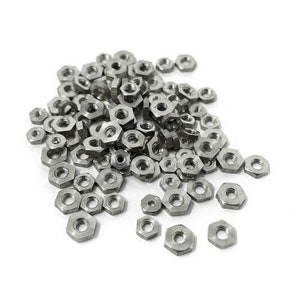 以下が含まれることがあります： 白い背景に散らばった、銀色の金属製の六角ナットの大きな山