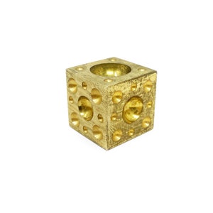 May include: A gold metal cube with a variety of round depressions on each side. The cube is used for shaping metal.