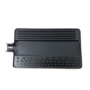May include: A black rectangular tray with a handle-like extension on one side. The tray features a series of parallel ridges on one end and evenly spaced circular indentations along the other. The surface has a glossy finish.