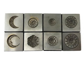 May include: Eight metal stamp blocks with different designs, including a crescent moon, a sun with a face, and a flower. The blocks are arranged in a grid pattern on a white background.