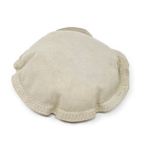 May include: A beige, suede-effect, round object with a scalloped edge. The edge features a double row of light-coloured stitching. The object appears to be a small, soft item, possibly a decorative piece or a component of a larger product.