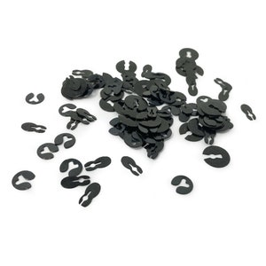 May include: A large pile of black metal retaining rings, also known as spring clips or snap rings, scattered on a white background.