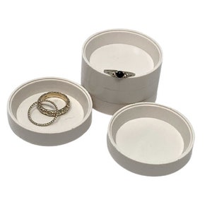 Op de afbeelding: Drie witte ronde ringdozen met deksels. Twee dozen hebben ringen erin. Eén doos is op een andere gestapeld.