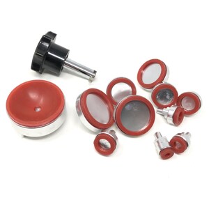 May include: A set of 10 silver and red tools for setting watch crystals. The tools include a knobbed handle with a metal rod, a round silver base with a red rubber top, and several smaller silver bases with red rubber tops.