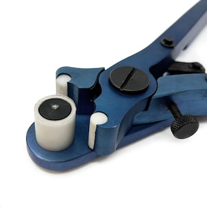May include: A close-up of a blue metal tool featuring a black screw and a white and black cylindrical component. The tool has a lever design with a black handle and a white base. The tool is designed for a specific purpose.