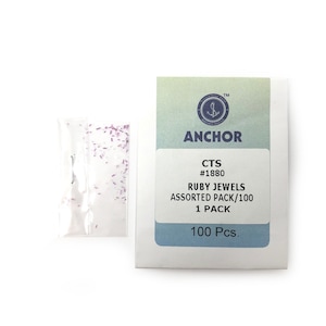 May include: A white packet of "ANCHOR" brand ruby jewels, assorted pack of 100 pieces. The packet is next to a small clear plastic bag containing small, rectangular, light purple jewels.
