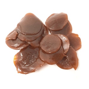 May include: A pile of brown, translucent, round, candy-like pieces. The pieces are stacked on top of each other and have a shiny, glossy finish.