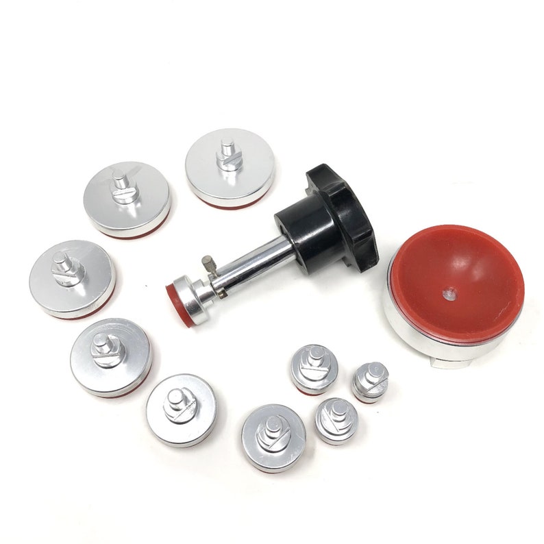 May include: A set of nine silver-colored suction cups with red rubber inserts, a black handle with a silver rod, and a red rubber dome. The suction cups are used for removing dents from car bodies.