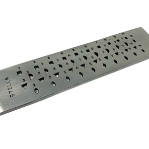 May include: A silver metal ring sizing gauge with a variety of sizes and shapes marked on it. The gauge is labelled "STELLA" on the side.