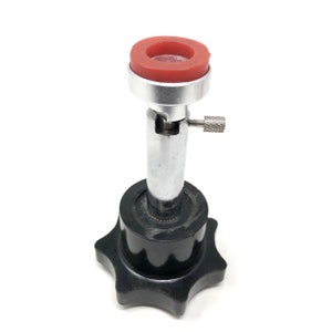 May include: A silver and black jewelry making tool with a red rubber ring on top. The tool has a knob on the bottom and a small screw on the side.