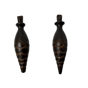 May include: Two dark brown wooden finials shaped like pine cones with a textured surface.