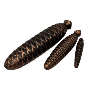May include: Three pine cone shaped metal ornaments in different sizes. The ornaments are a dark brown colour with a copper finish.