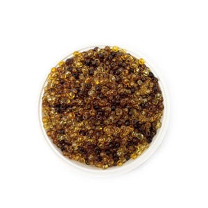 以下が含まれることがあります： 白く丸いお皿に、小さな琥珀色のビーズがたくさん入っています。ビーズは明るい黄色から濃い茶色まで色合いが異なり、質感のある外観になっています。ビーズは、おそらく工芸品やジュエリー作りに使用されます。