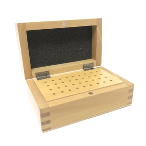 May include: A wooden box with a hinged lid and a foam-lined interior. The box has a grid of holes on the bottom for storing small items.