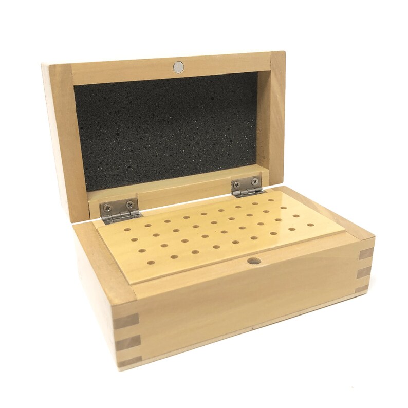 May include: A wooden box with a hinged lid and a foam-lined interior. The box has a grid of holes on the bottom for storing small items.