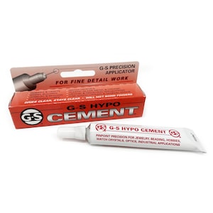 Peut inclure: Un tube de colle G-S Hypo Cement avec un applicateur de précision. Le tube est blanc avec du texte rouge et noir qui indique "G-S Hypo Cement" et "Précision optimale pour la bijouterie, la perlage, les loisirs, les cristaux de montre, l'optique, les applications industrielles".