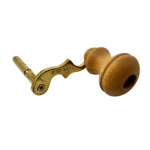 May include: A vintage wooden and brass crank handle. The handle has a light brown, rounded wooden grip and a brass arm with the text "2-50-NO 1". The brass arm has a hexagonal end.