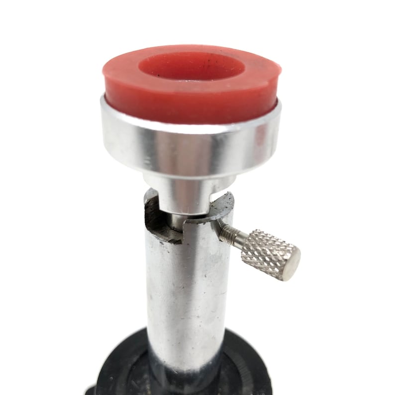 May include: A silver and black metal ring holder with a red rubber top. The holder has a small knob on the side to adjust the height.