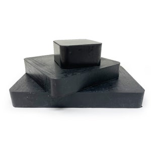 May include: Three black rubber blocks stacked on top of each other. The blocks are square and have rounded edges.