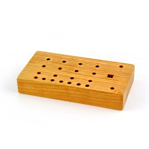 May include: A wooden block with a grid of holes drilled into the top surface. The block is light brown in colour and has a square hole in the centre.