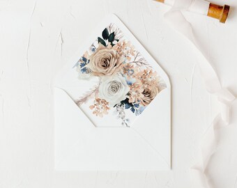 May include: A white envelope with a floral design on the flap. The design features a bouquet of beige, white, and blue flowers with green leaves. The envelope is lying on a white surface.