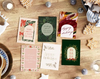 May include: A collection of holiday greeting cards with various designs and text, including "Merry Christmas & Happy New Year" and "Happy Holidays." The cards are arranged on a wooden surface with decorative elements like gingerbread cookies and candles.