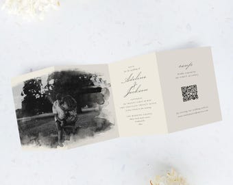 May include: A tri-fold wedding invitation with a black and white photo and elegant script. The invitation includes the names Adeline & Jackson, wedding date, and a QR code. White flowers and greenery are in the background.