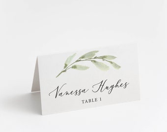 May include: White place card with a green watercolor leaf design. The text reads "Vanessa Hughes, Table 1."
