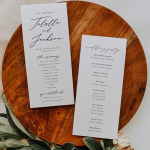 May include: Two white cards with black text. The first card is a wedding ceremony program for Jebelle and Jackson. The second card lists the wedding party members, including the bride's parents, groom's parents, maid of honor, best man, bridesmaids, groomsmen, flower girl, and ring bearer.