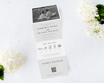 May include: A folded wedding invitation with a black and white photo of a couple. The invitation includes the names Kimberly Marie and Frankie Michael, event details, and a QR code. White flowers and greenery are in the background.