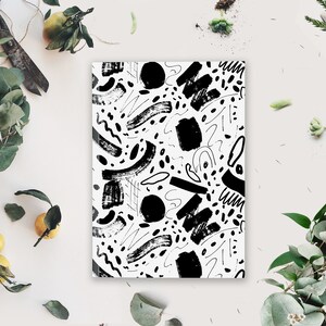 May include: Black and white abstract pattern with brushstrokes and dots on a white background. The pattern is printed on a notebook.