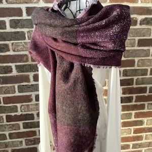 May include: A burgundy and gray plaid scarf with a shimmery finish. The scarf has a fringed edge.