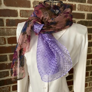 May include: A sheer scarf with a floral print in shades of pink, purple, and brown. The scarf is tied around a white shirt.
