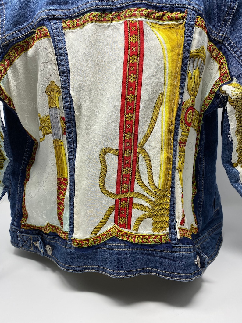 Peut inclure: Une veste en jean bleue avec un design patchwork mettant en vedette un tissu blanc avec un motif or et rouge. Le motif comprend une corde, des fleurs et un motif or.