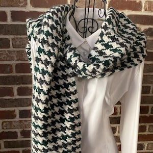 May include: A black, white, and green patterned scarf with a houndstooth design. The scarf is draped over a white shirt with a collar.