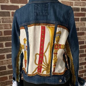 Peut inclure: Une veste en jean bleue avec une doublure en tissu &agrave; motifs blancs et dor&eacute;s. Le tissu pr&eacute;sente un motif r&eacute;p&eacute;t&eacute; d'une corde, d'une trompette et d'un motif d&eacute;coratif.