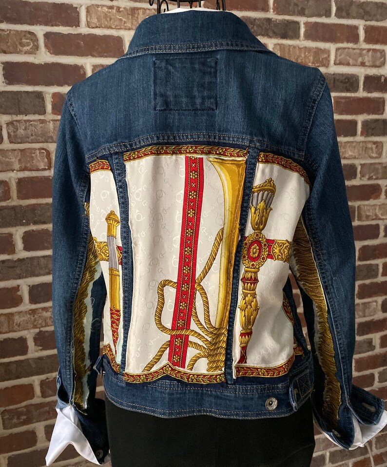 Peut inclure: Une veste en jean bleue avec une doublure en tissu &agrave; motifs blancs et dor&eacute;s. Le tissu pr&eacute;sente un motif r&eacute;p&eacute;t&eacute; d'une corde, d'une trompette et d'un motif d&eacute;coratif.