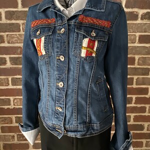 Peut inclure: Une veste en jean bleue avec des d&eacute;tails brod&eacute;s rouges, blancs et dor&eacute;s sur les poches avant et le col.
