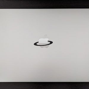 May include: A silver laptop with a black Apple logo surrounded by a black ring.